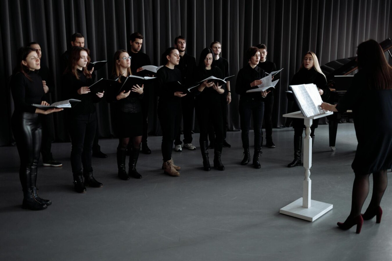 A choir group rehearsing with music sheets under a conductor's direction indoors, focusing on harmony.